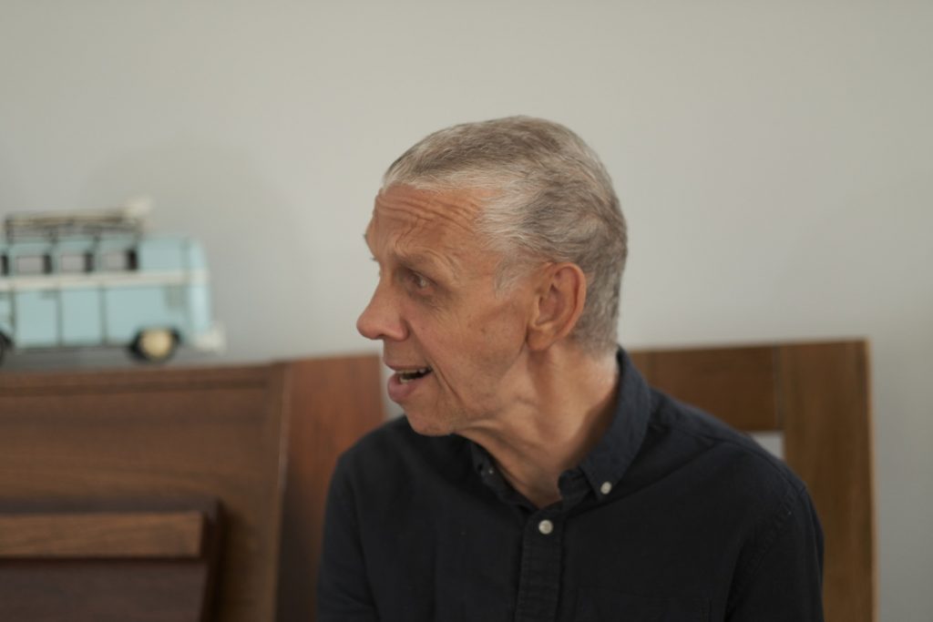 Man with short hair and a black shirt looks to the left, smiling.