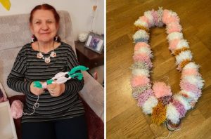 On the left, a woman is smiling at the camera and holding a white and green pom pom maker. On the right is a string of pom poms in white, pink and grey.