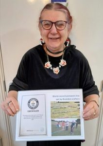 A woman wearing a black top holding a certificate for the world record for the longest line of pom-poms.