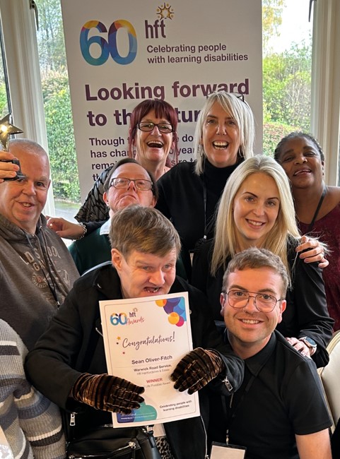 8 people all smiling. One is in the centre holding a certificate