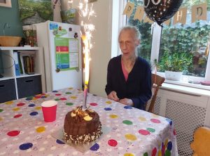 Pat sat at a table in front of a chocolate cake with a sparkler on it.