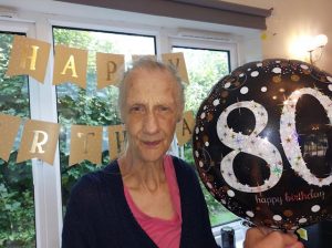 Pat holding a black balloon with the number '80' on it.