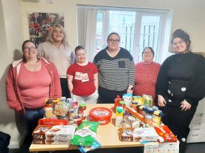Six women standing behind a table of foodbank donations