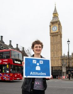 Rachael standing outside Big Ben holding a sign that reads 'Attitudes'