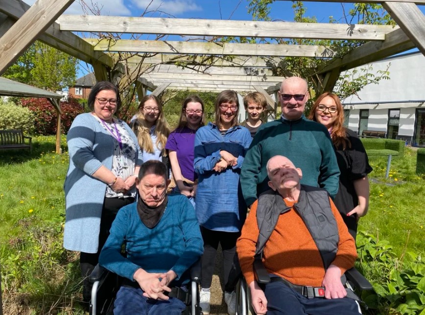 The residents alongside the staff and visiting students enjoying a group photo in the sunny gardens together