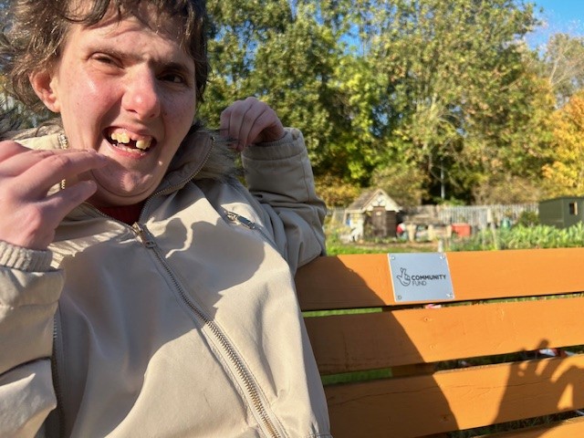 Naz sitting on the new bench. It has a metal plaque with the community fund logo on it. 