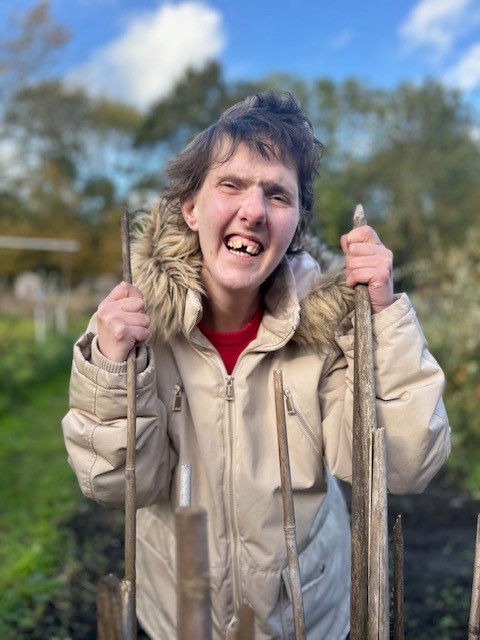 Naz, one of the volunteer gardeners, holds onto two fence sticks and smiles.